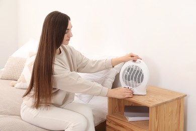 Woman turning on modern electric fan heater at home