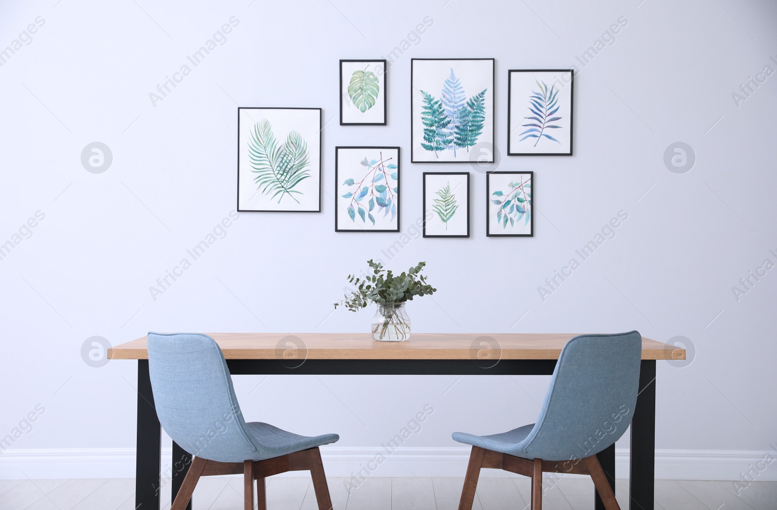 Photo of Stylish room interior with modern table, chairs and paintings of tropical leaves. Idea for design