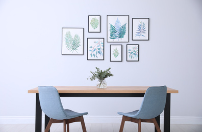 Stylish room interior with modern table, chairs and paintings of tropical leaves. Idea for design