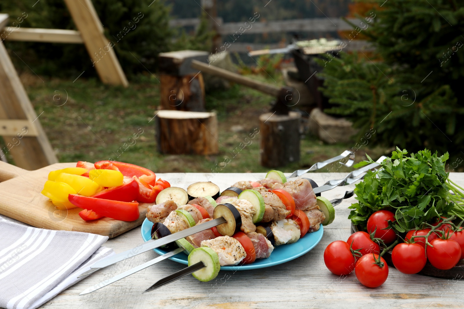 Photo of Metal skewers with raw marinated meat and vegetables on wooden table outdoors