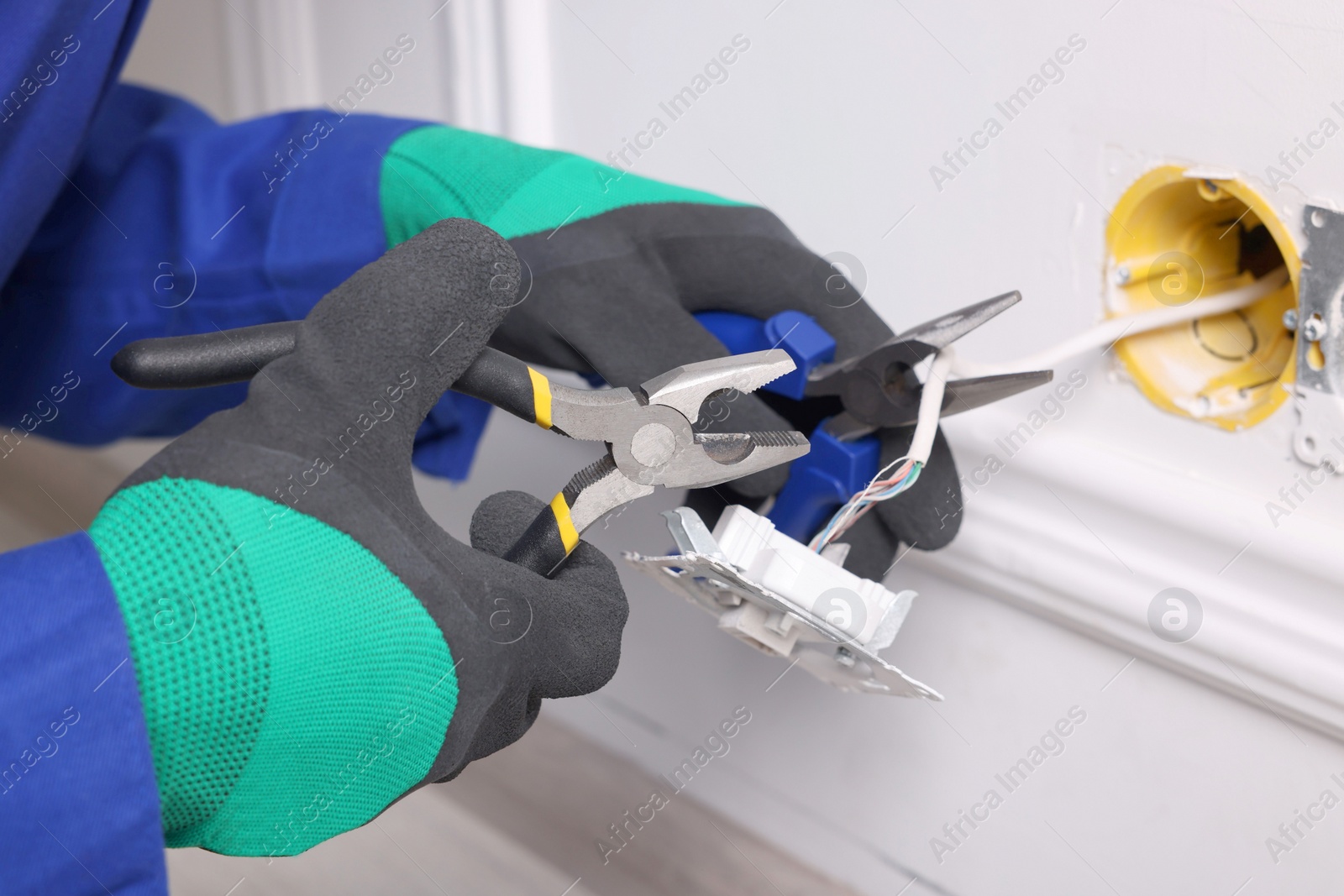 Photo of Professional repairman fixing power sockets with pliers indoors, closeup