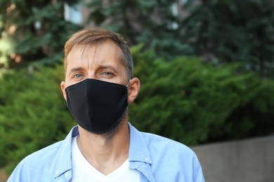 Photo of Man wearing handmade cloth mask outdoors, space for text. Personal protective equipment during COVID-19 pandemic