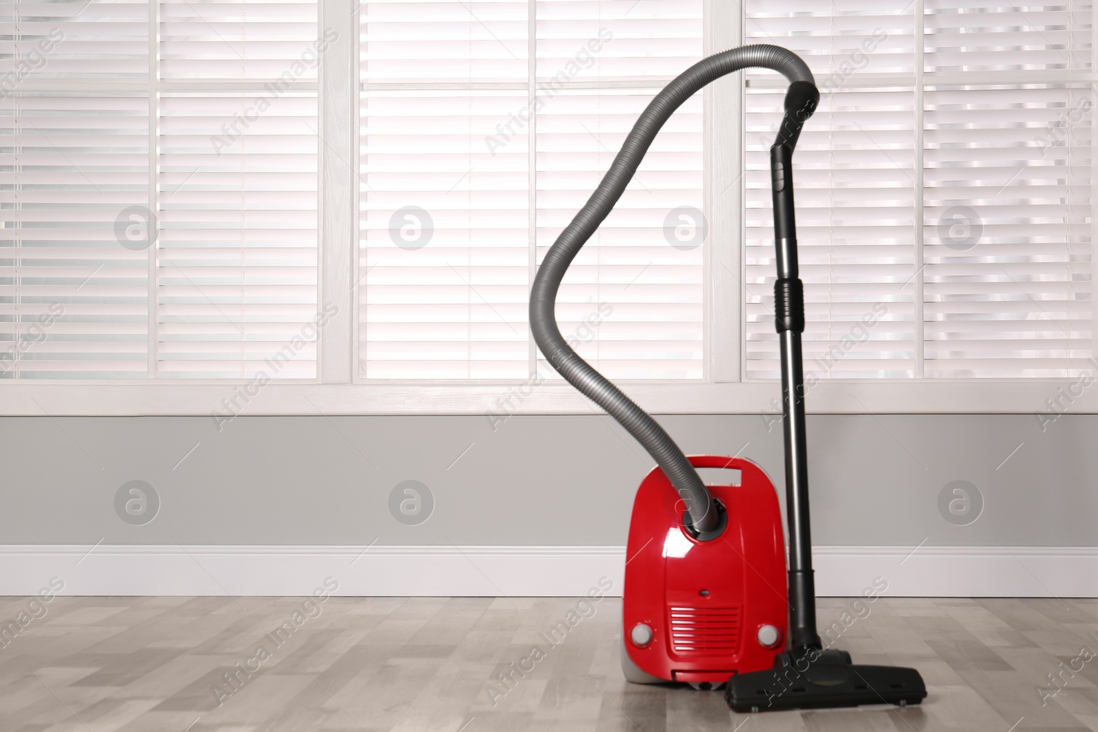 Photo of Modern red vacuum cleaner on floor indoors, space for text