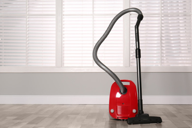 Modern red vacuum cleaner on floor indoors, space for text