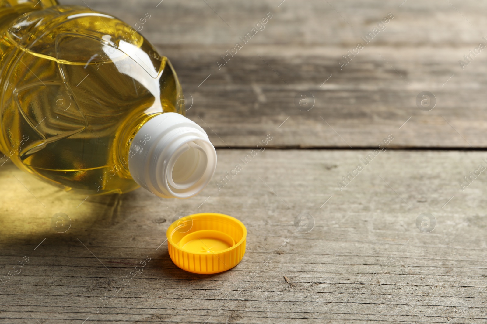 Photo of Plastic bottle of cooking oil on wooden table. Space for text