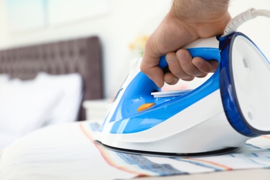 Man ironing clothes on board indoors, space for text. Household chores