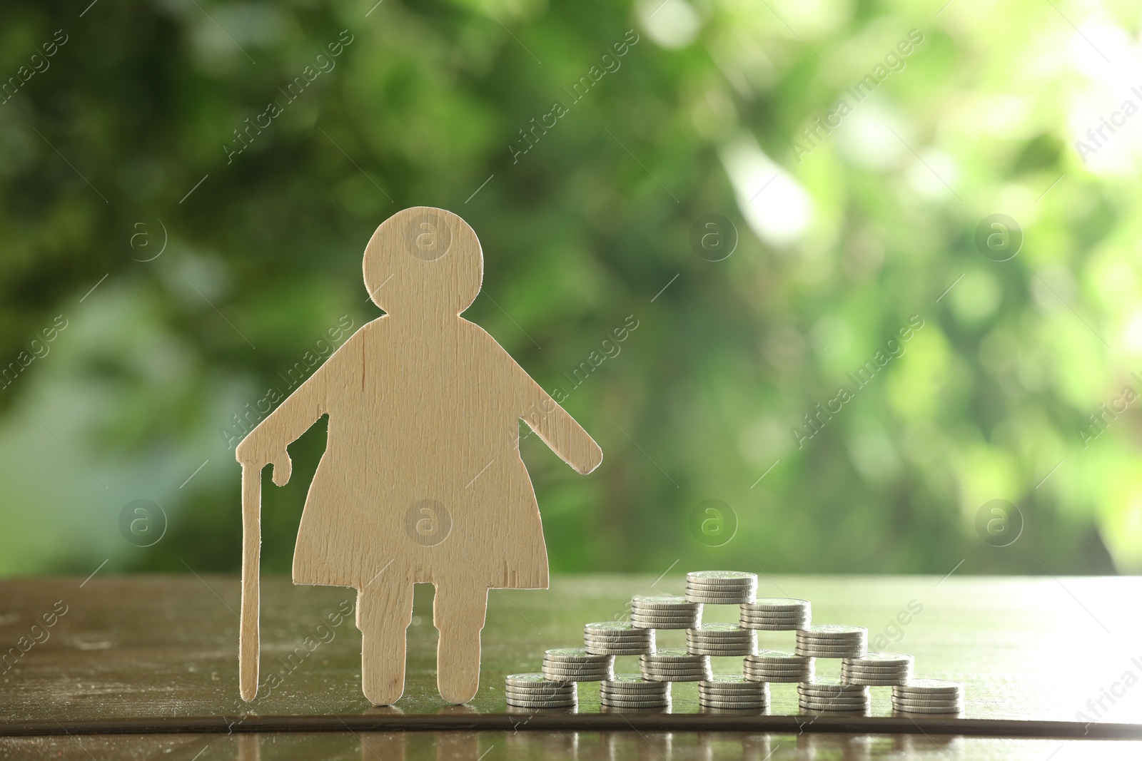 Photo of Pension savings. Figure of senior woman and stacked coins on wooden table outdoors