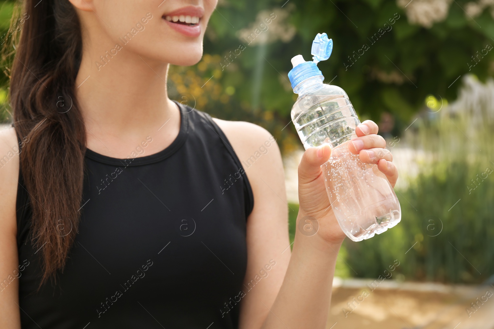 Photo of Young woman with bottle of pure water outdoors, closeup