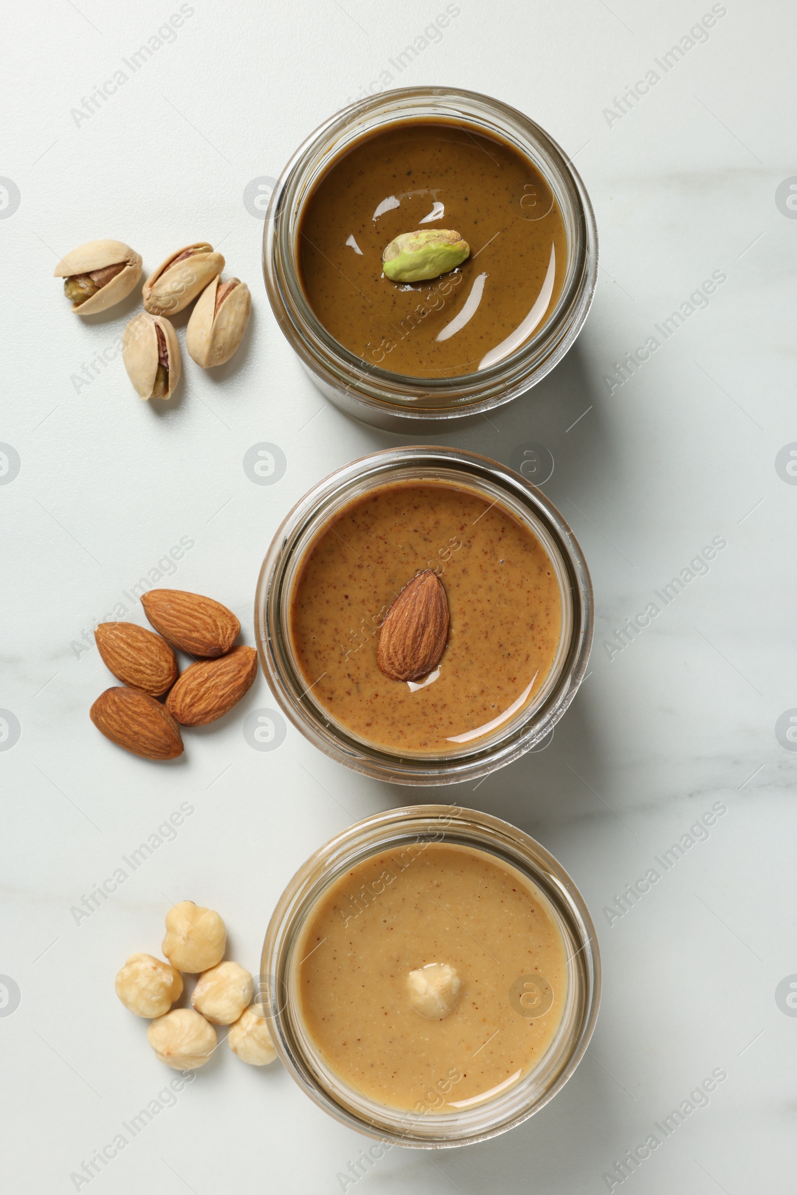 Photo of Tasty nut butters in jars and raw nuts on white marble table, flat lay