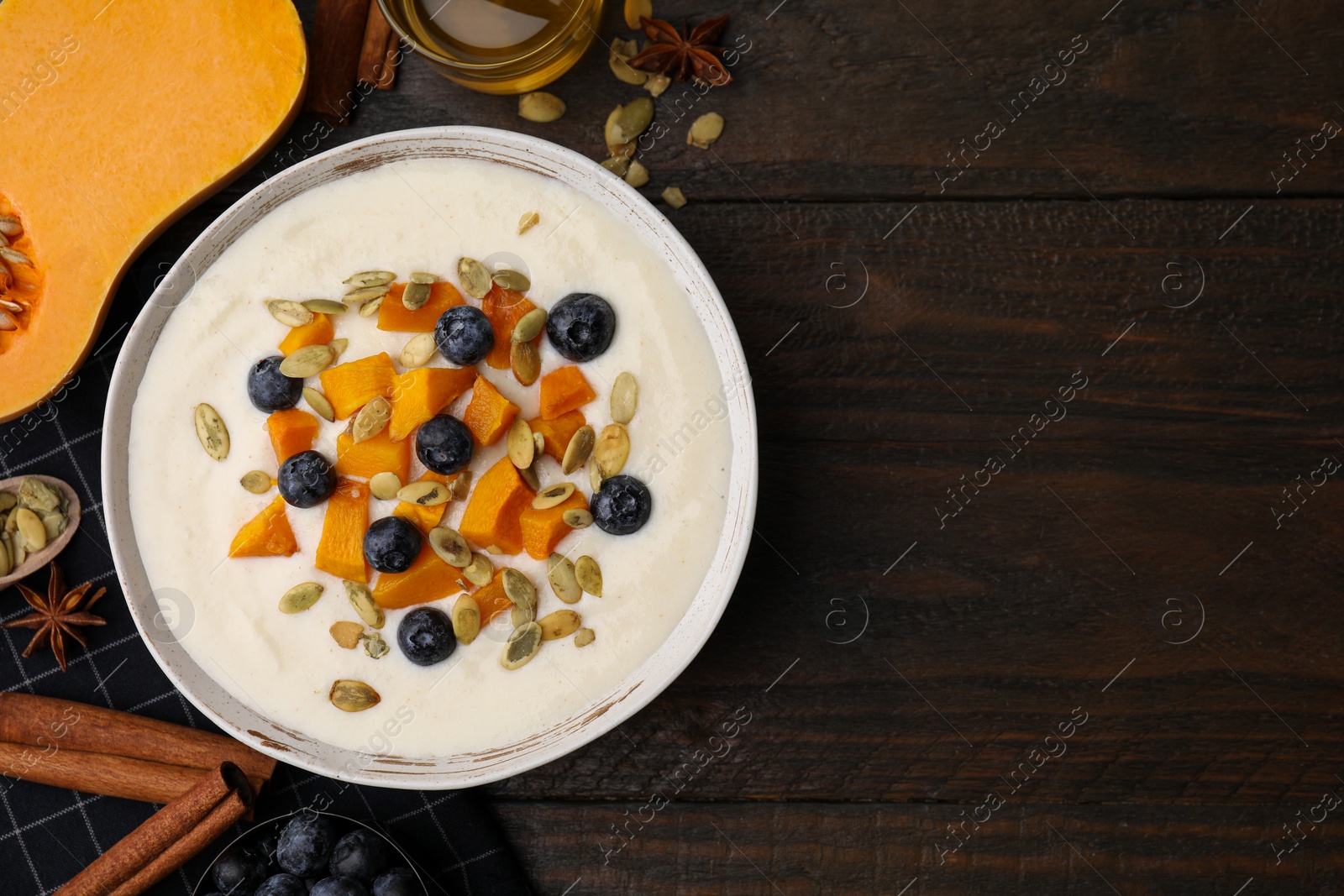 Photo of Bowl of delicious semolina pudding with blueberries, pumpkin and ingredients on wooden table, flat lay. Space for text