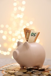 Photo of Piggy bank with euro banknote and coins on grey table against blurred lights