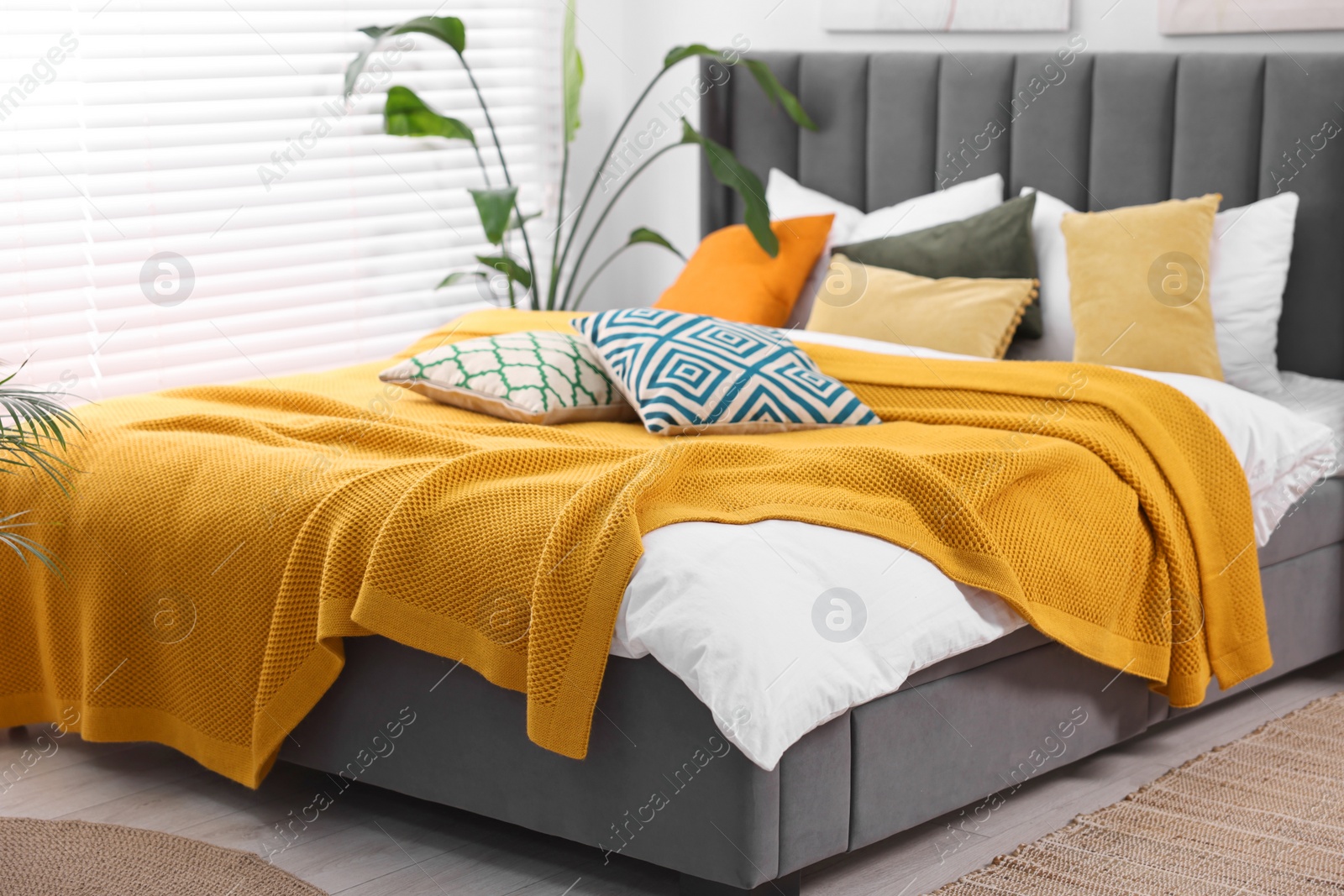 Photo of Bright plaid and colorful pillows on bed in stylish bedroom. Interior design