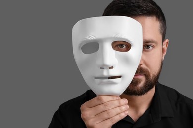 Multiple personality concept. Man covering face with mask on grey background. Space for text