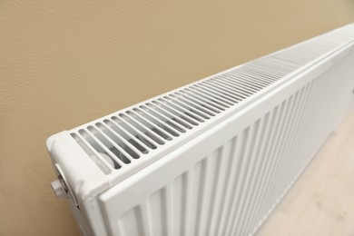 Photo of Modern radiator on beige wall, closeup. Central heating system
