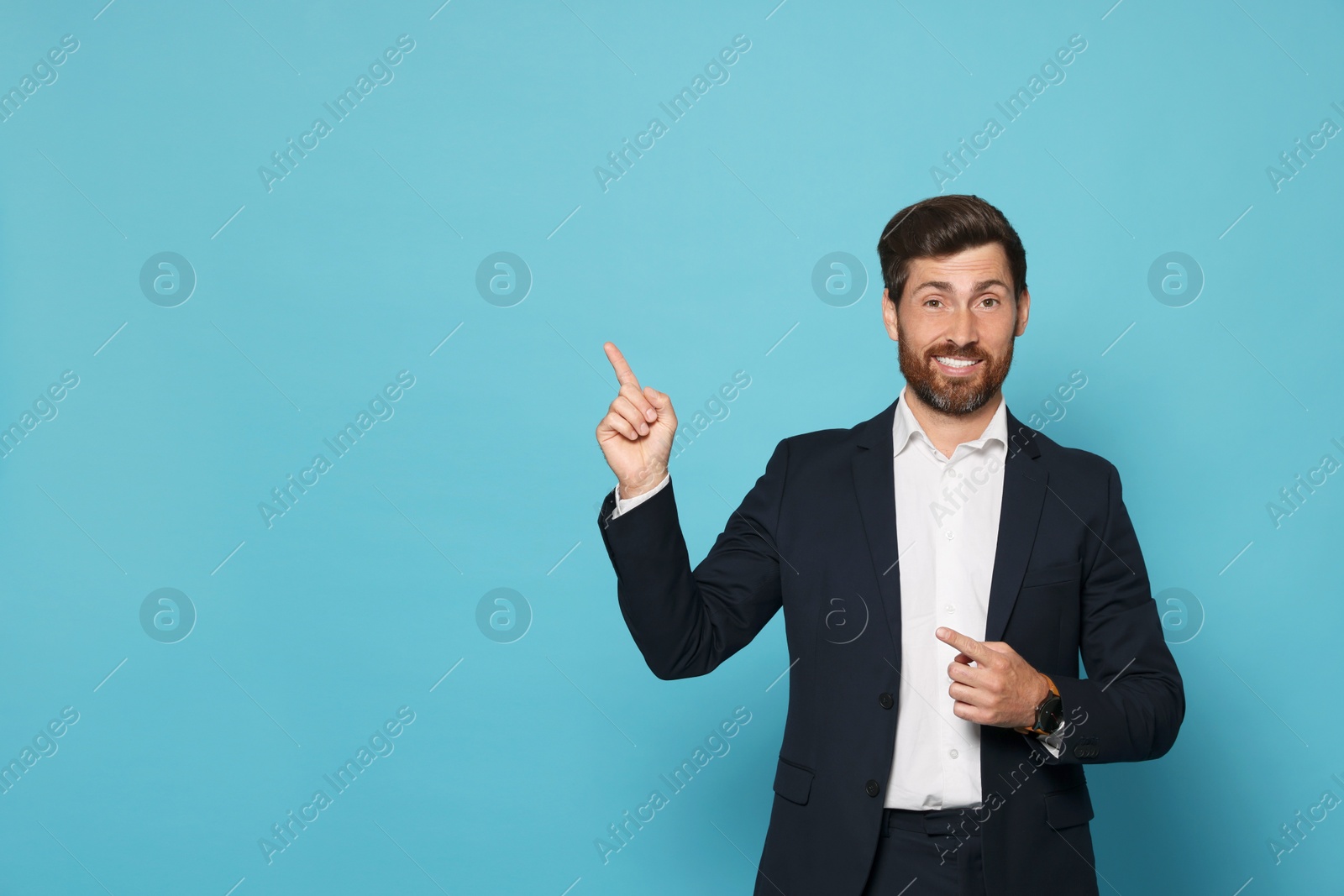 Photo of Smiling bearded man pointing index finger up on light blue background. Space for text