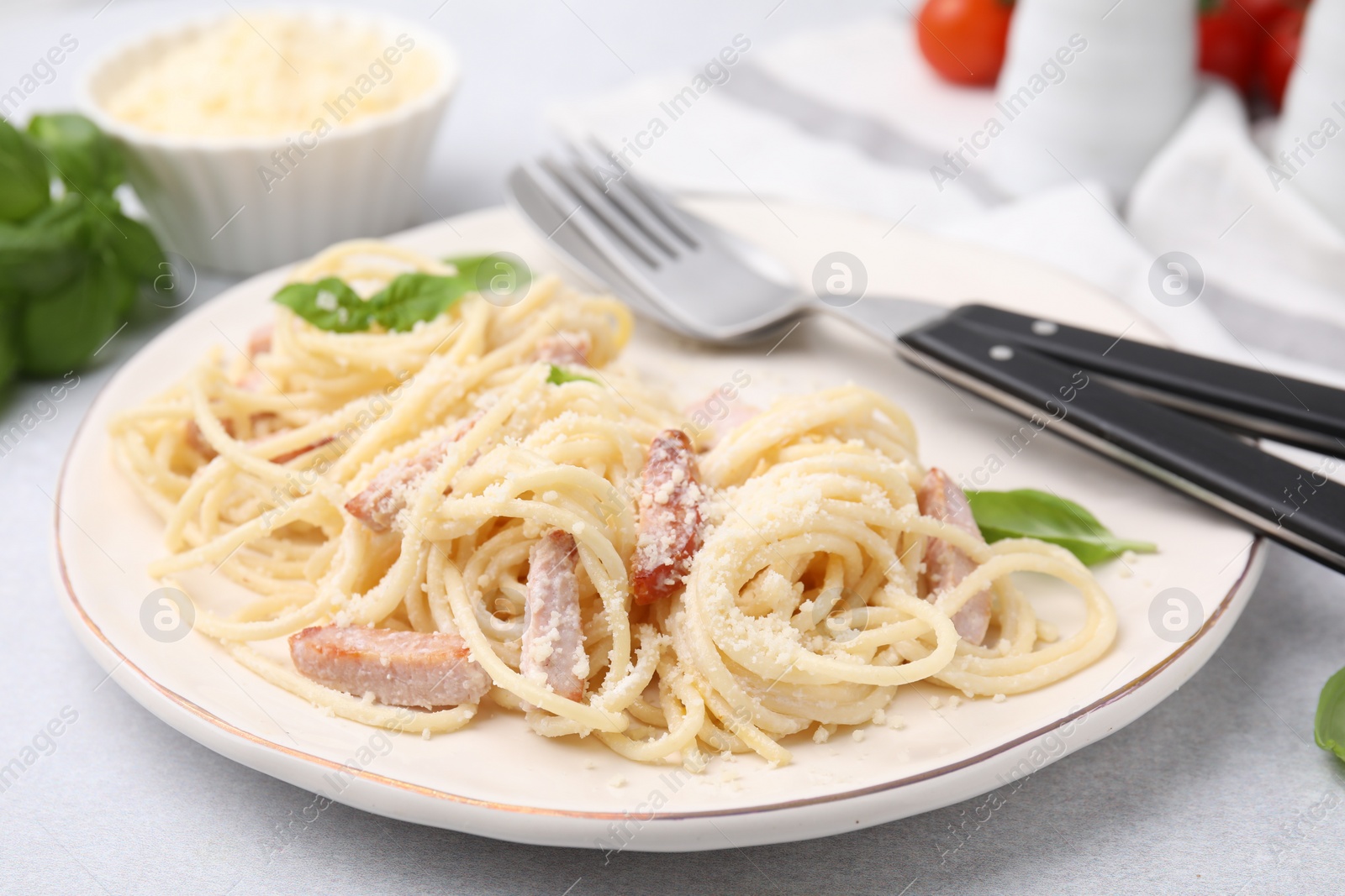 Photo of Plate of tasty pasta Carbonara with basil leaves on light grey table, closeup