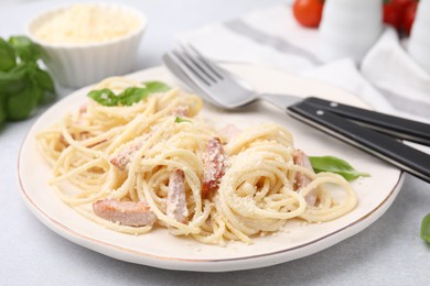 Photo of Plate of tasty pasta Carbonara with basil leaves on light grey table, closeup