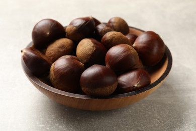 Photo of Roasted edible sweet chestnuts in bowl on light grey table, closeup