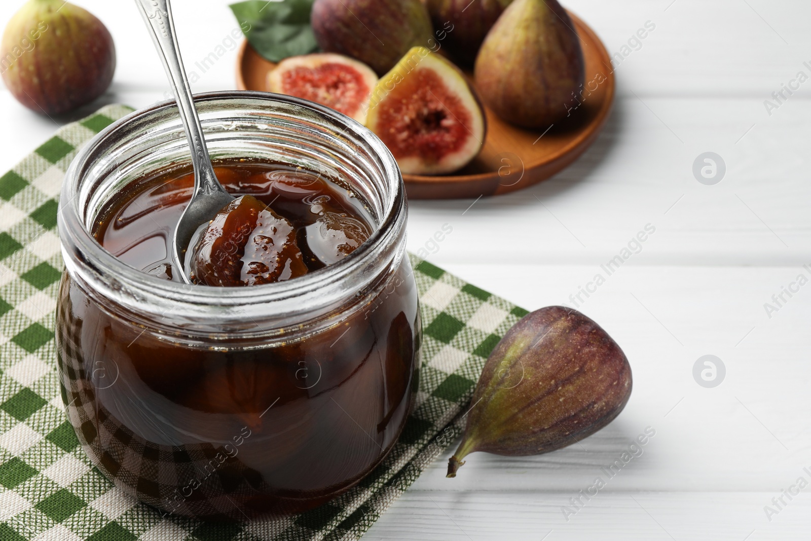 Photo of Jar of tasty sweet jam and fresh figs on white wooden table. Space for text