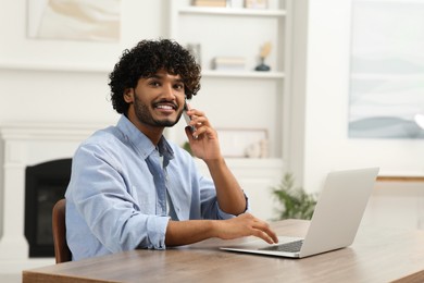 Handsome smiling man talking on smartphone in room, space for text