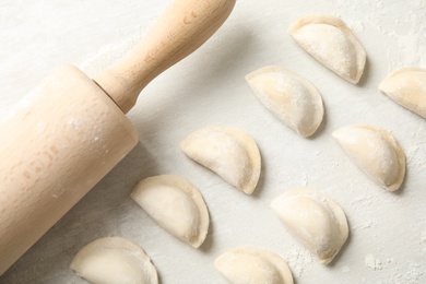 Photo of Raw dumplings and rolling pin on light background, top view. Process of cooking