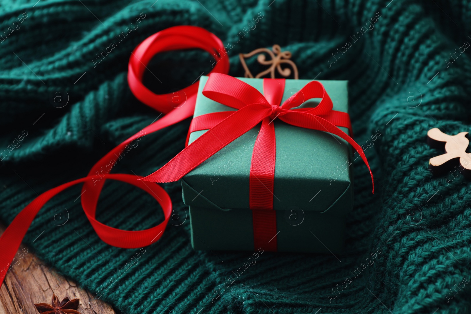 Photo of Christmas gift box on green knitted cloth, closeup