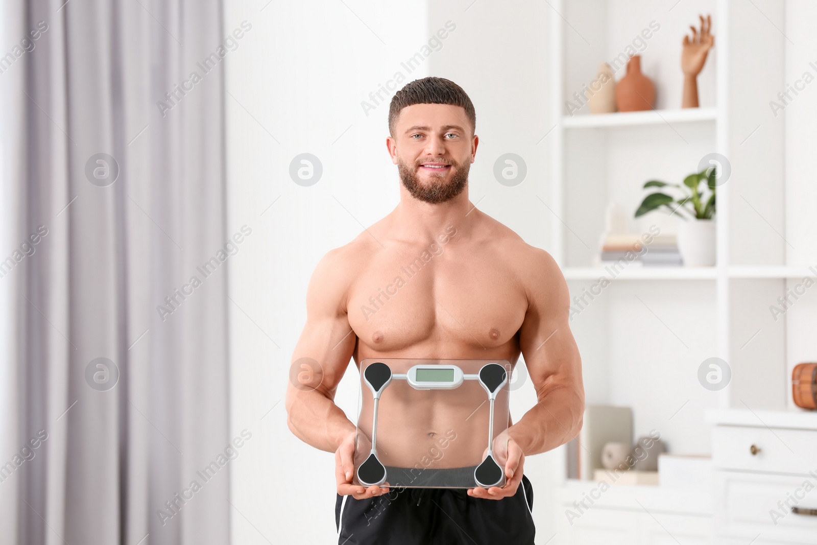 Photo of Portrait of happy athletic man with scales at home. Weight loss concept