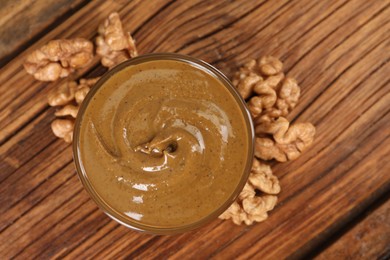 Delicious nut butter in bowl and walnuts on wooden table, top view