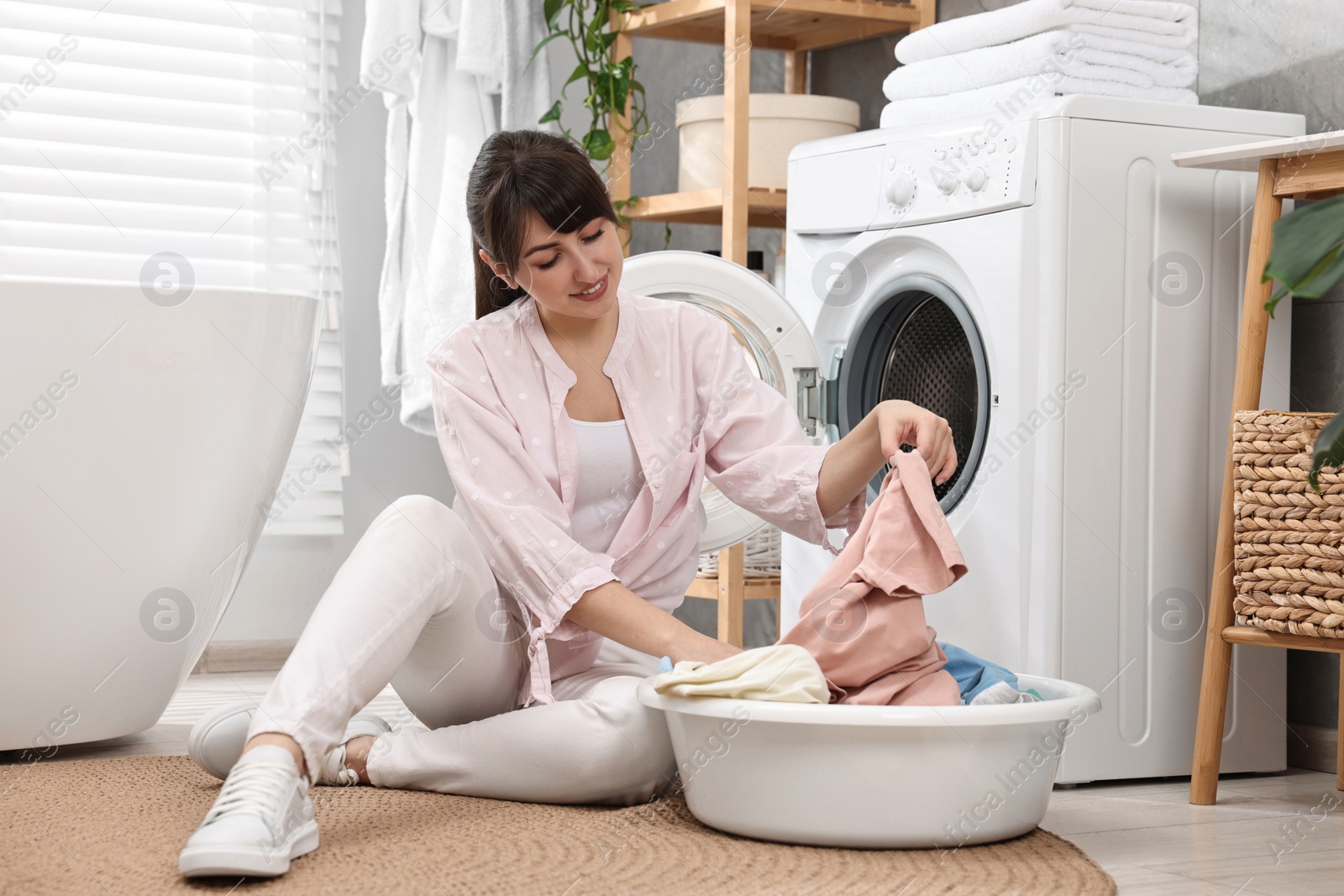 Photo of Happy young housewife with laundry near washing machine at home