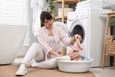Happy young housewife with laundry near washing machine at home