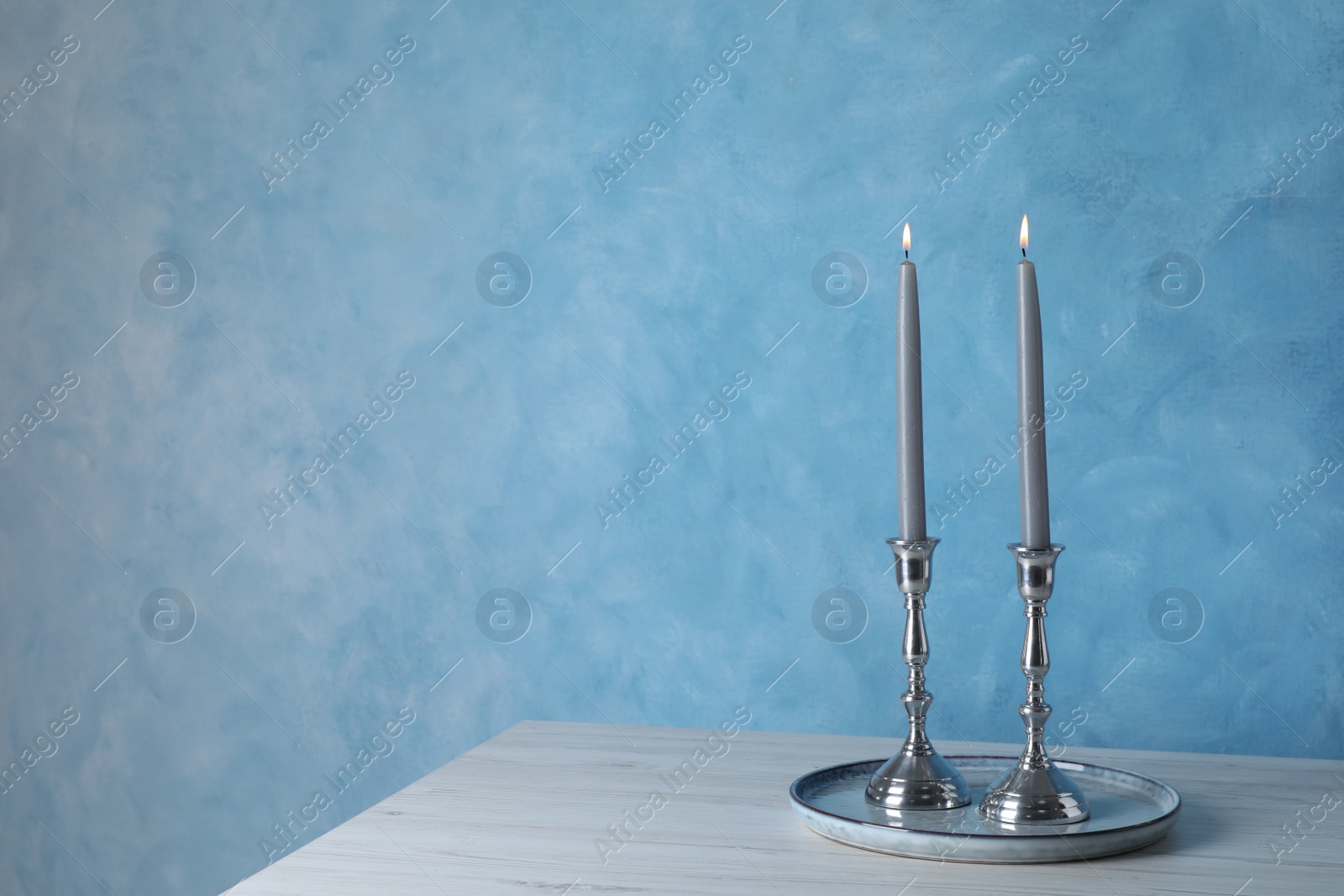 Photo of Holders with burning candles on wooden table near light blue wall, space for text