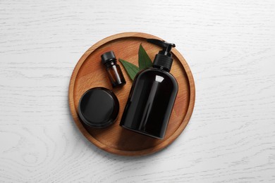 Different cosmetic products and leaves on white wooden table, top view