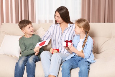 Photo of Cute little children presenting their mother with gifts on sofa at home