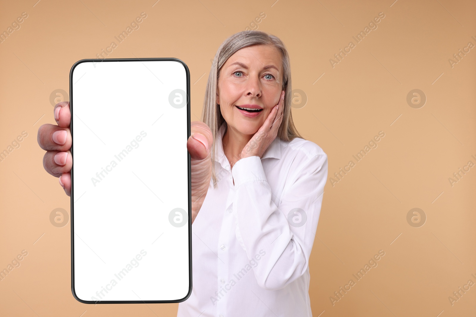 Image of Mature woman showing mobile phone with blank screen on beige background. Mockup for design
