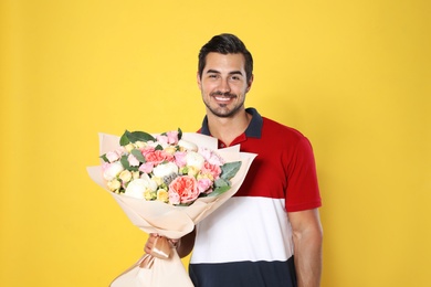 Photo of Young handsome man with beautiful flower bouquet on yellow background