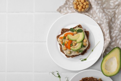 Photo of Tasty vegan sandwich with avocado, chickpeas and bell pepper on white tiled table, flat lay. Space for text