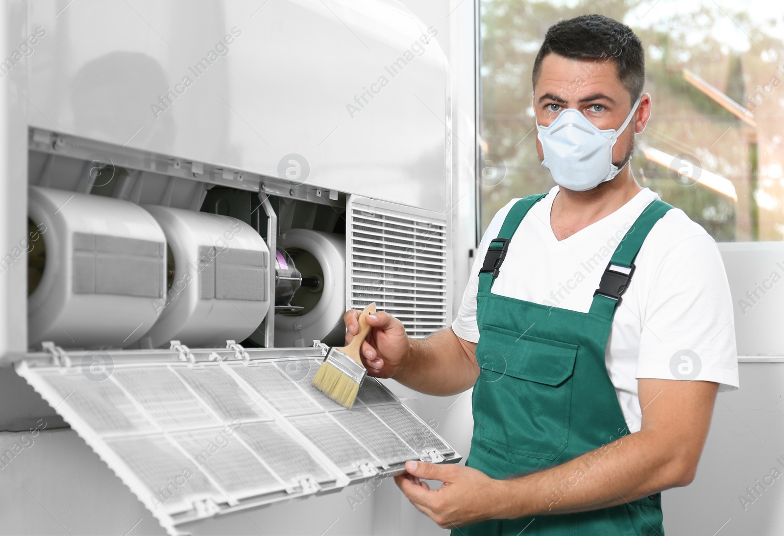 Photo of Professional male technician cleaning air conditioner indoors. Repair and maintenance