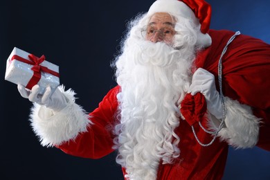 Photo of Santa Claus with Christmas gift and bag on dark blue background