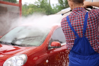 Photo of Male worker cleaning vehicle with high pressure water jet at car wash