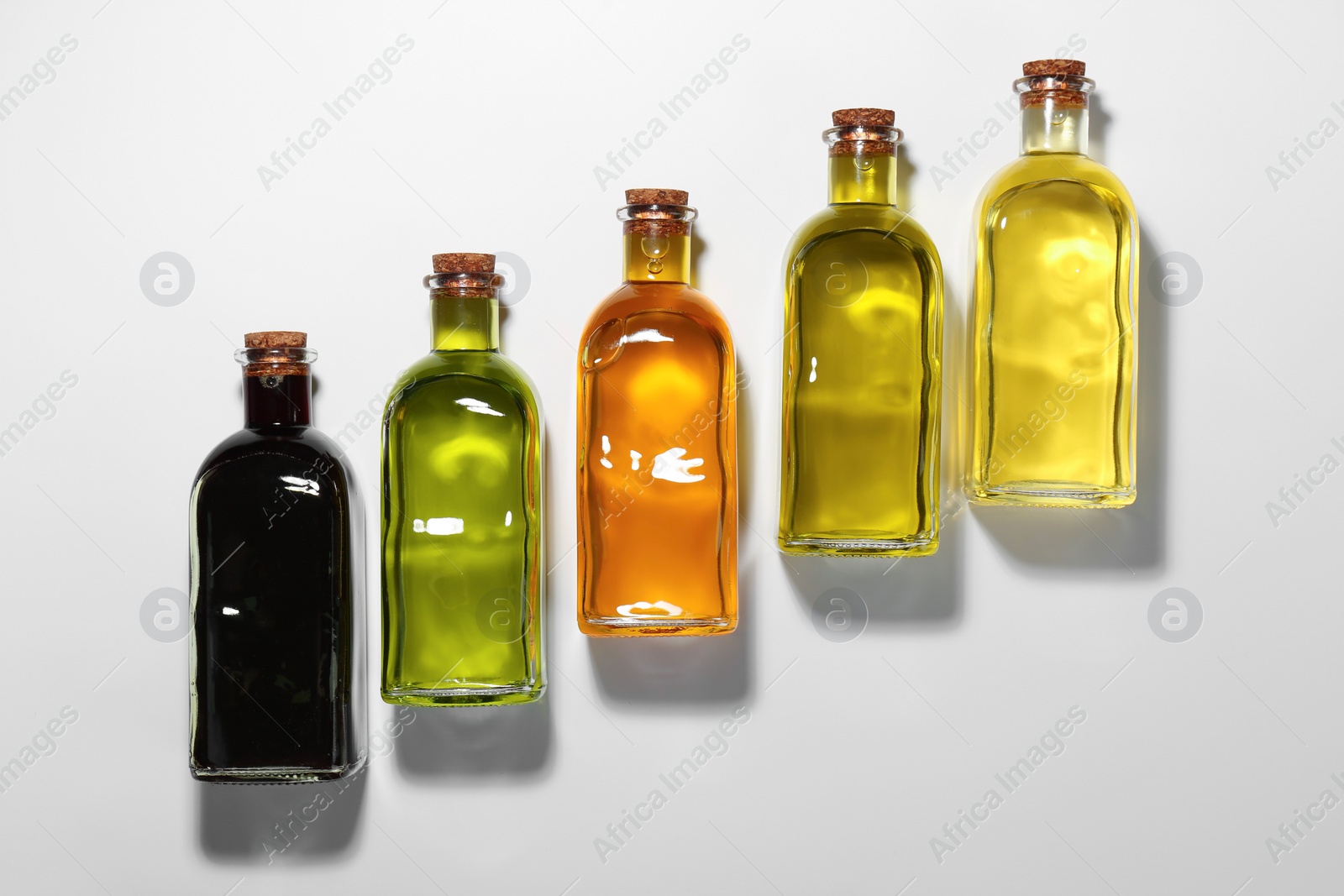 Photo of Vegetable fats. Different cooking oils in glass bottles on white background, flat lay