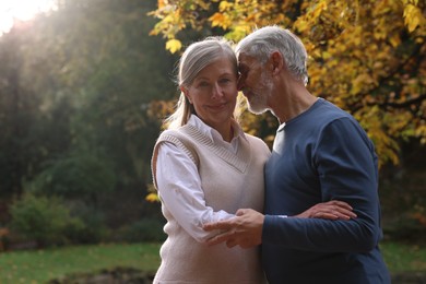 Photo of Portrait of affectionate senior couple in autumn park, space for text