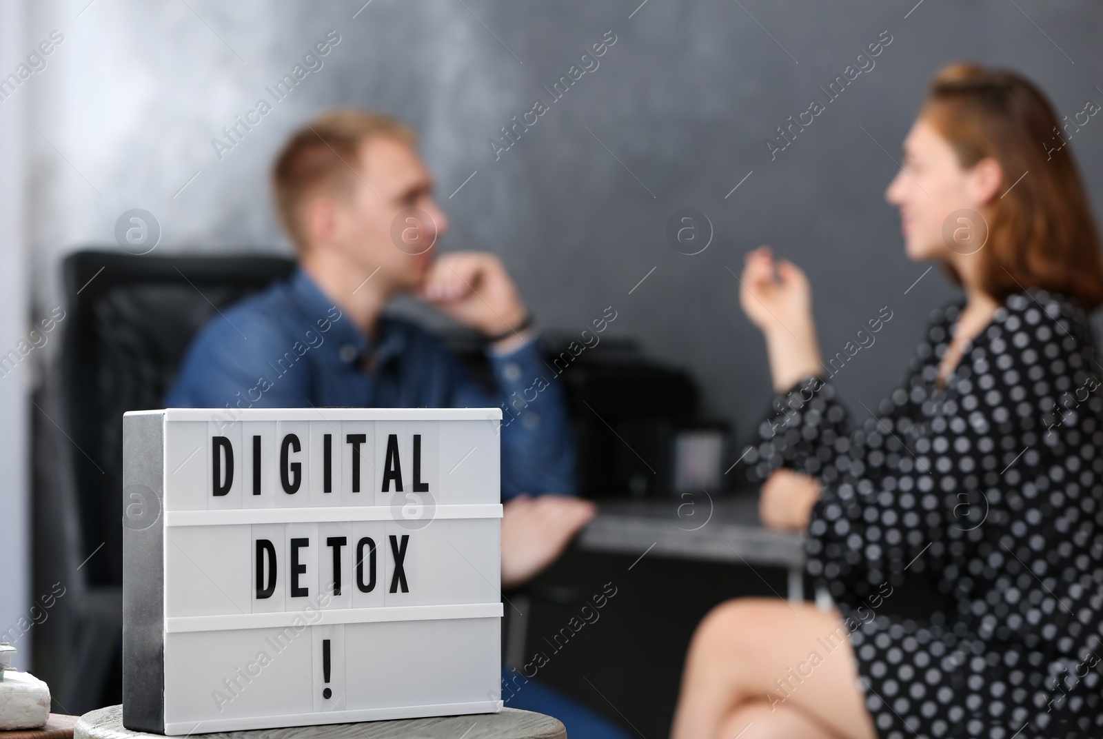 Photo of Colleagues chatting in office, focus on lightbox with phrase DIGITAL DETOX