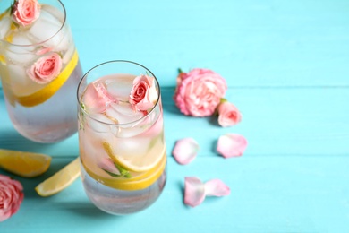 Photo of Tasty refreshing lemon drink with roses on light blue wooden