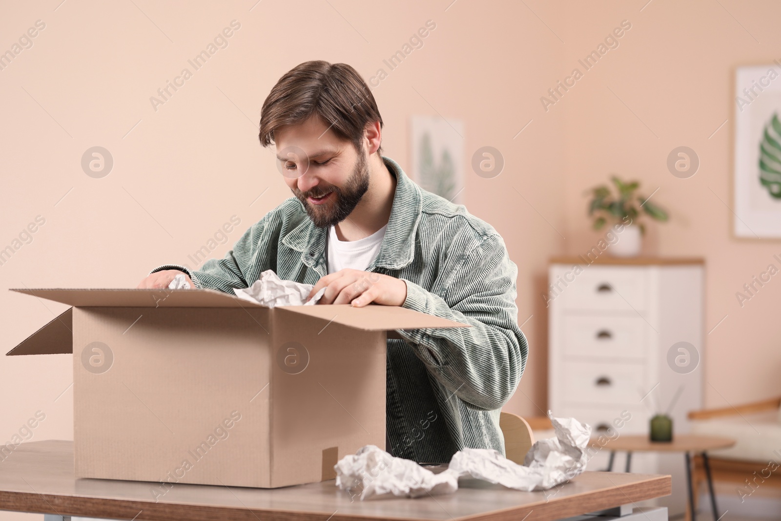 Photo of Happy man opening parcel at home. Internet shopping