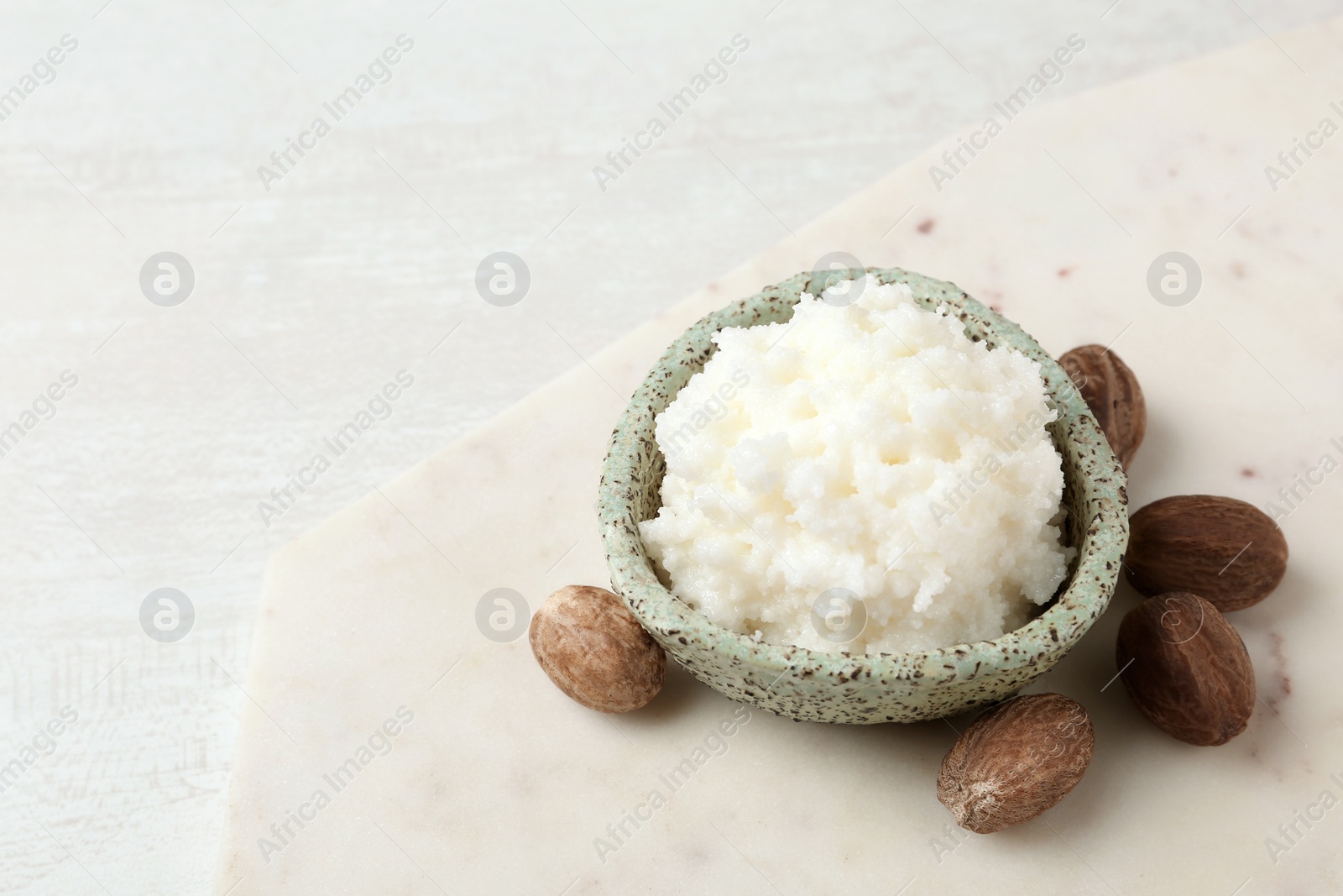 Photo of Shea butter in bowl and nuts on table. Space for text