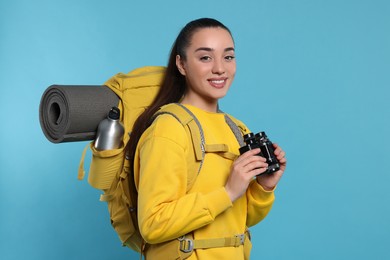Photo of Young woman with backpack and binoculars on light blue background. Active tourism