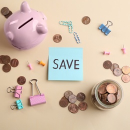 Photo of Note with word SAVE, piggy bank and coins on beige background, flat lay