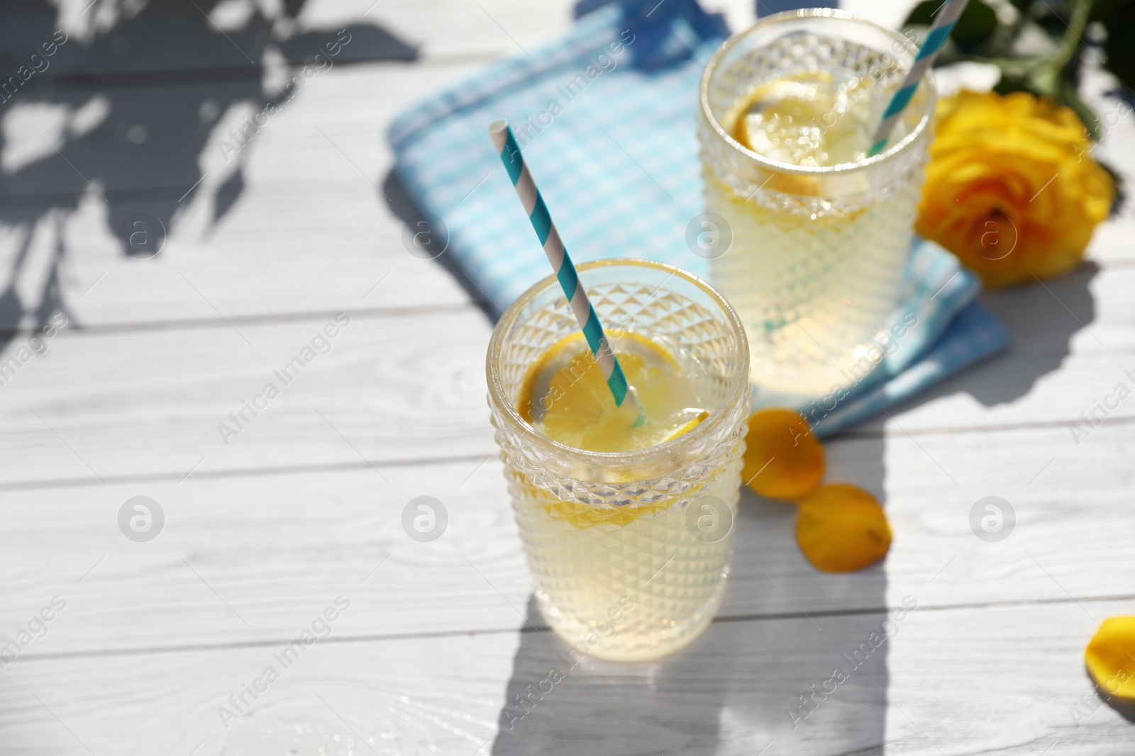 Photo of Glasses of refreshing lemonade and beautiful yellow rose on white wooden table. Space for text