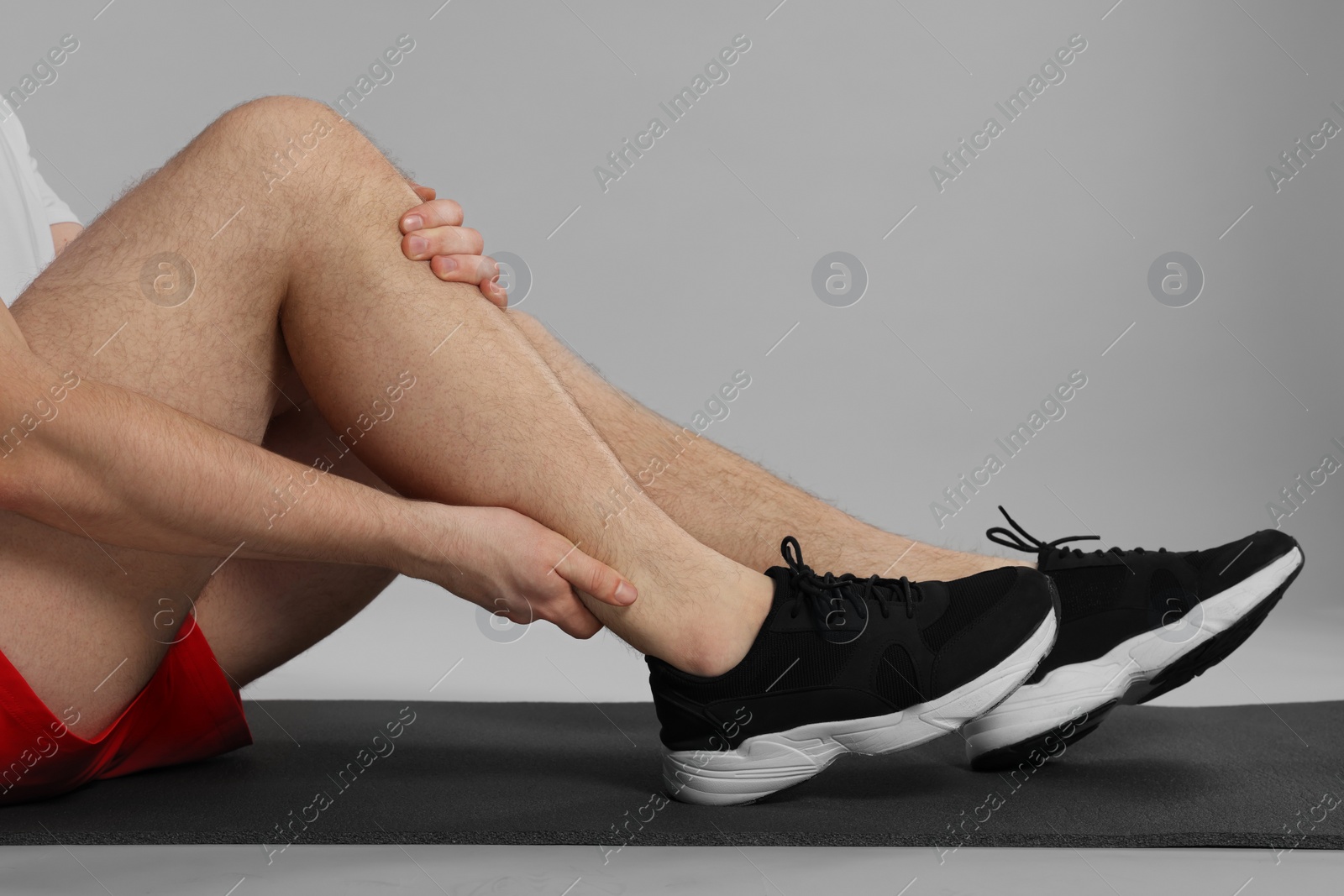 Photo of Man suffering from leg pain on mat against grey background, closeup