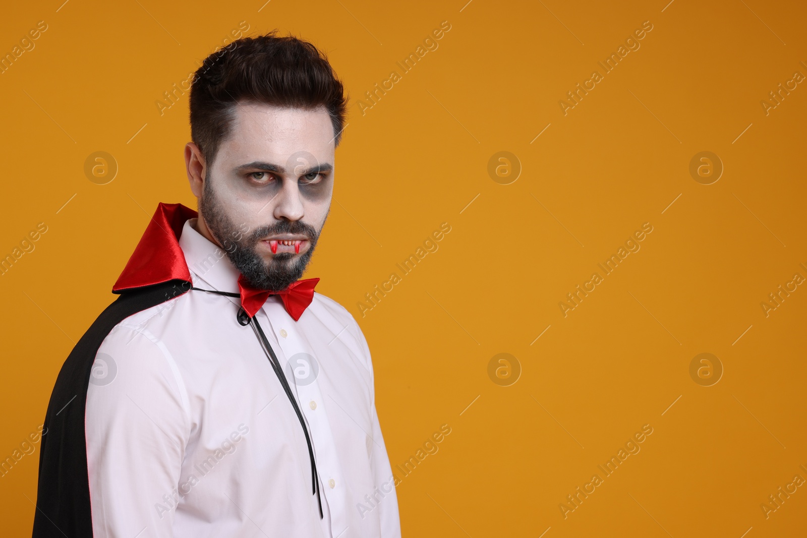 Photo of Man in scary vampire costume with fangs on orange background, space for text. Halloween celebration